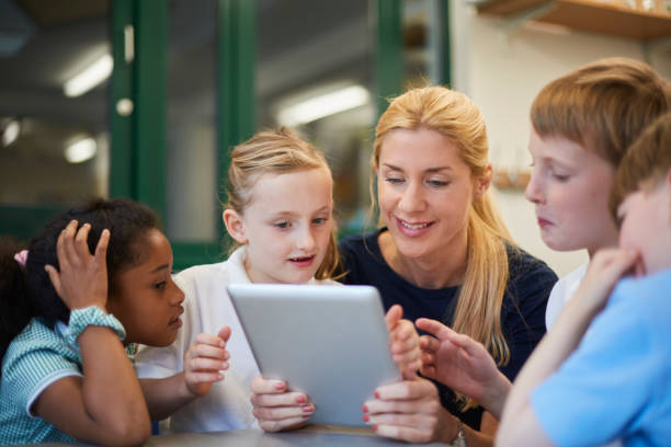 Une enseignante et un groupe d'élèves regroupés autour d'une tablette numérique