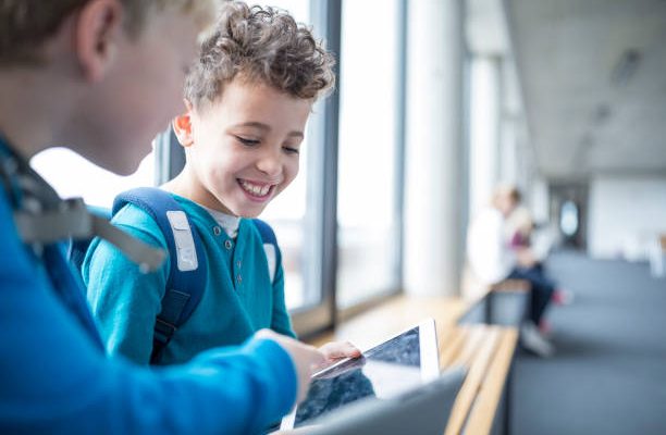 Deux enfants qui jouent sur une tablette numérique dans un couloir d'école